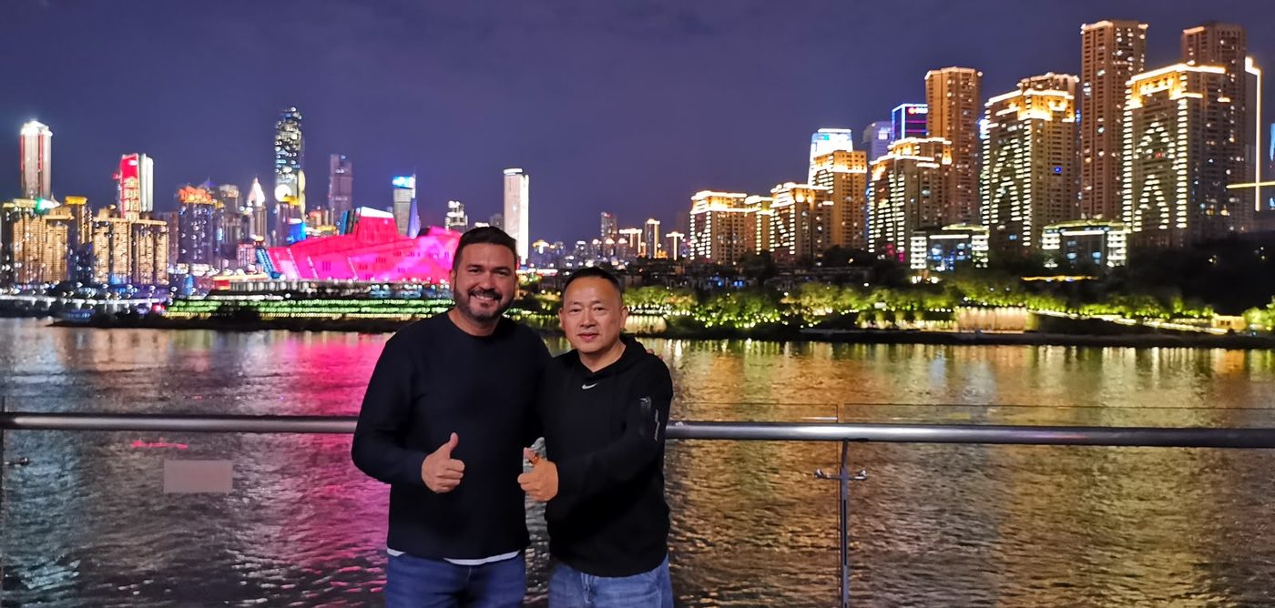 Arcelino Calado ao lado de um parceiro comercial chinês, com a paisagem urbana da China ao fundo